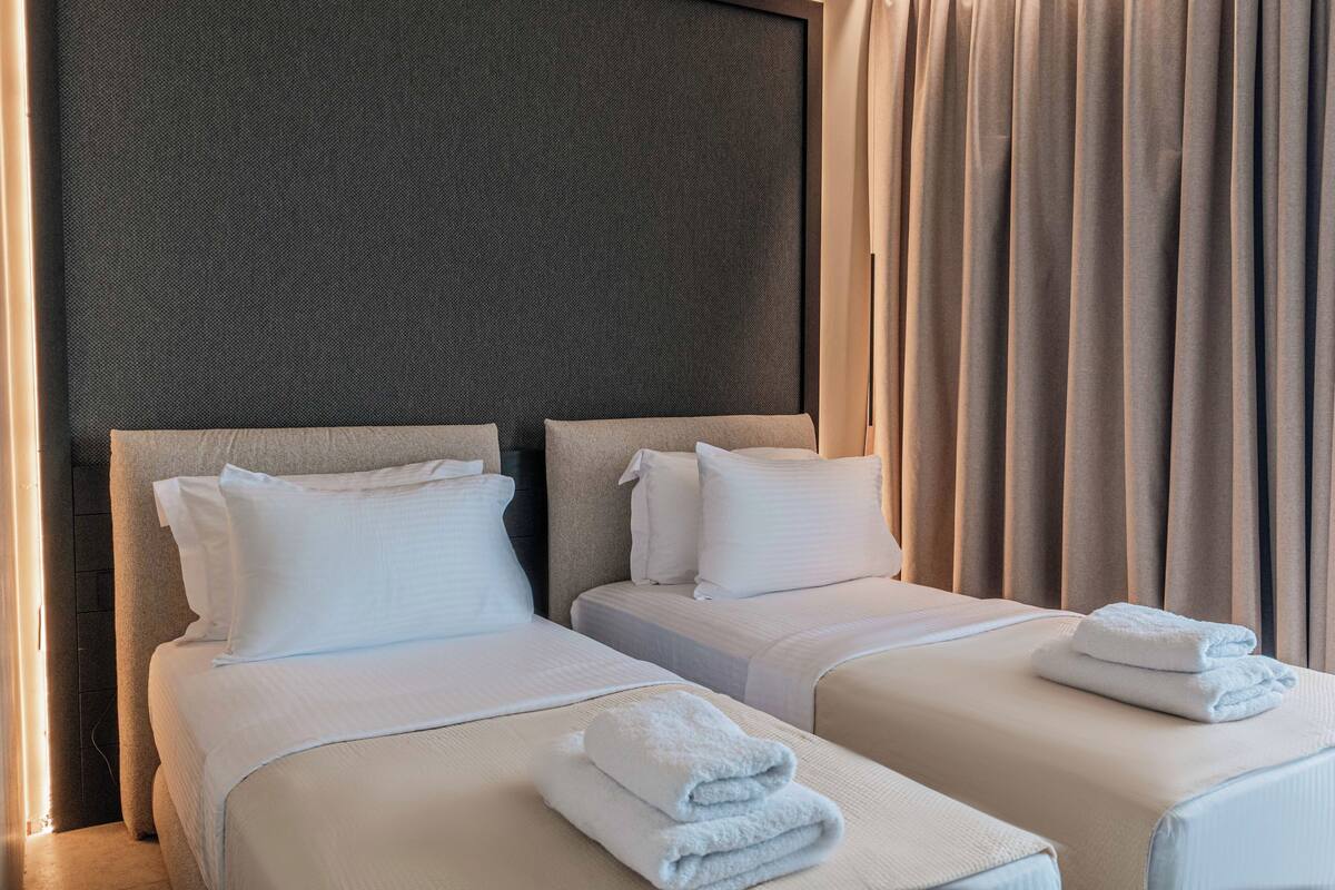 A hotel room with two beds, each with white bedding and pillows, and a neatly folded towel on the beds.