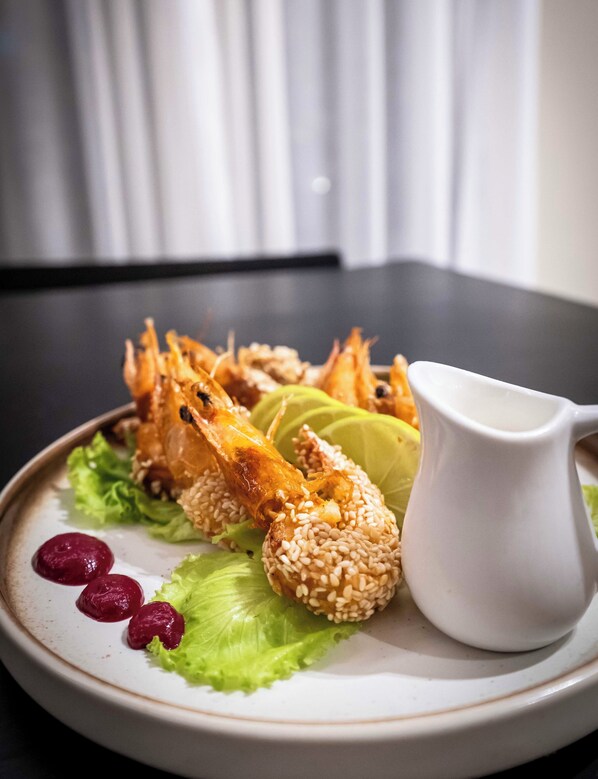 A plate of food with shrimp, sesame balls, and a small pitcher of sauce, served on a white plate with green lettuce and red berries.