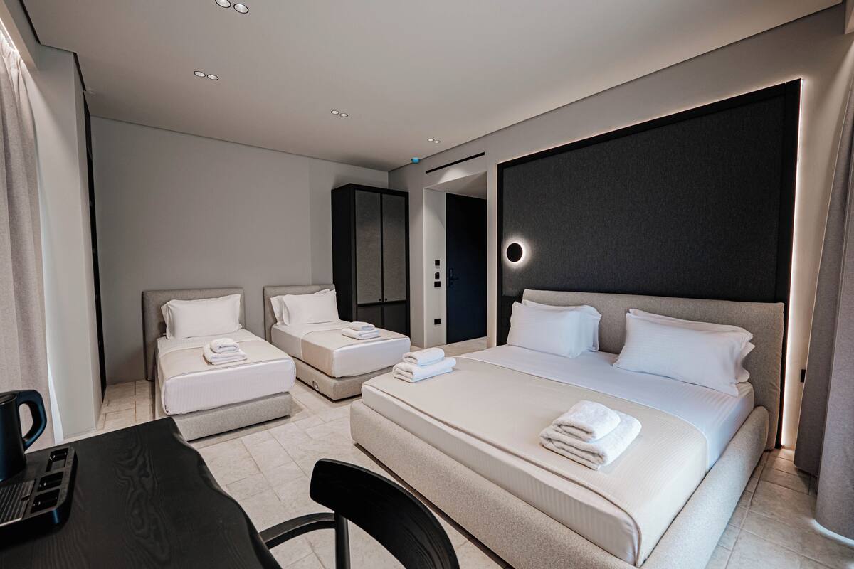 A modern hotel room with a large bed, two smaller beds, a desk, and a chair.