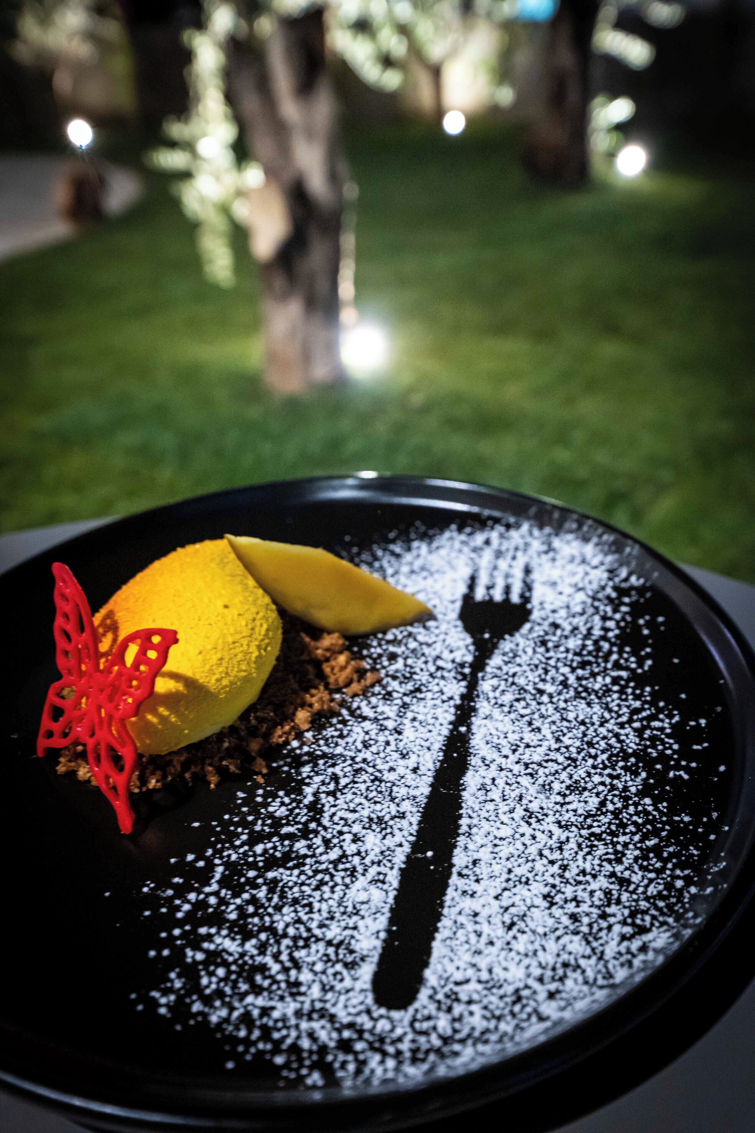 A dessert on a black plate with powdered sugar, a fork, and a red decorative element.