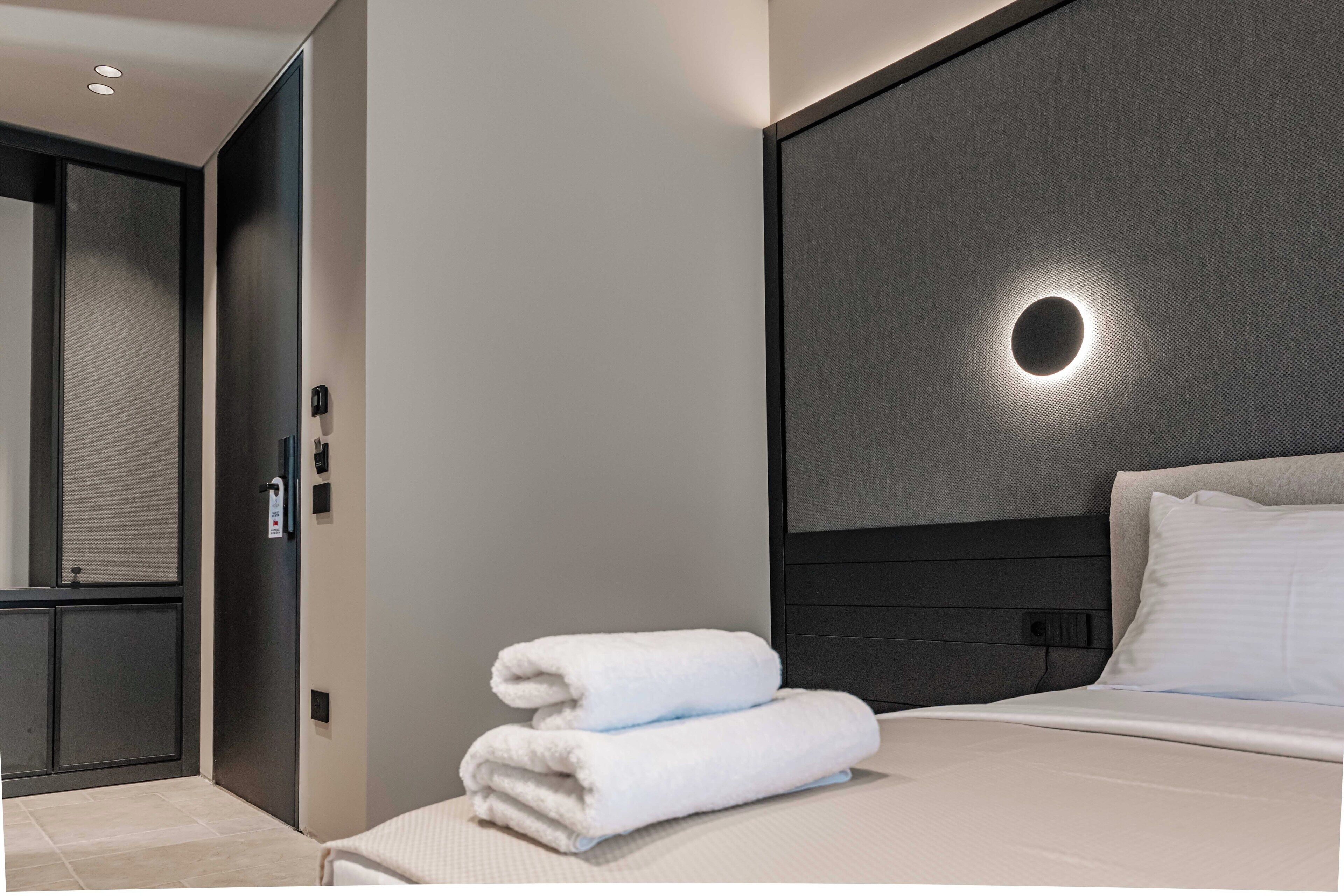 Un moderno cuarto de hotel con una cama bien hecha, un espejo grande y una lámpara fijada a la pared.