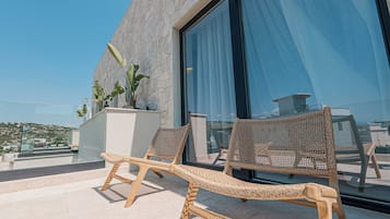 Un balcon avec des fauteuils de jardin en osier, une plante en pot et une vue sur la ville.