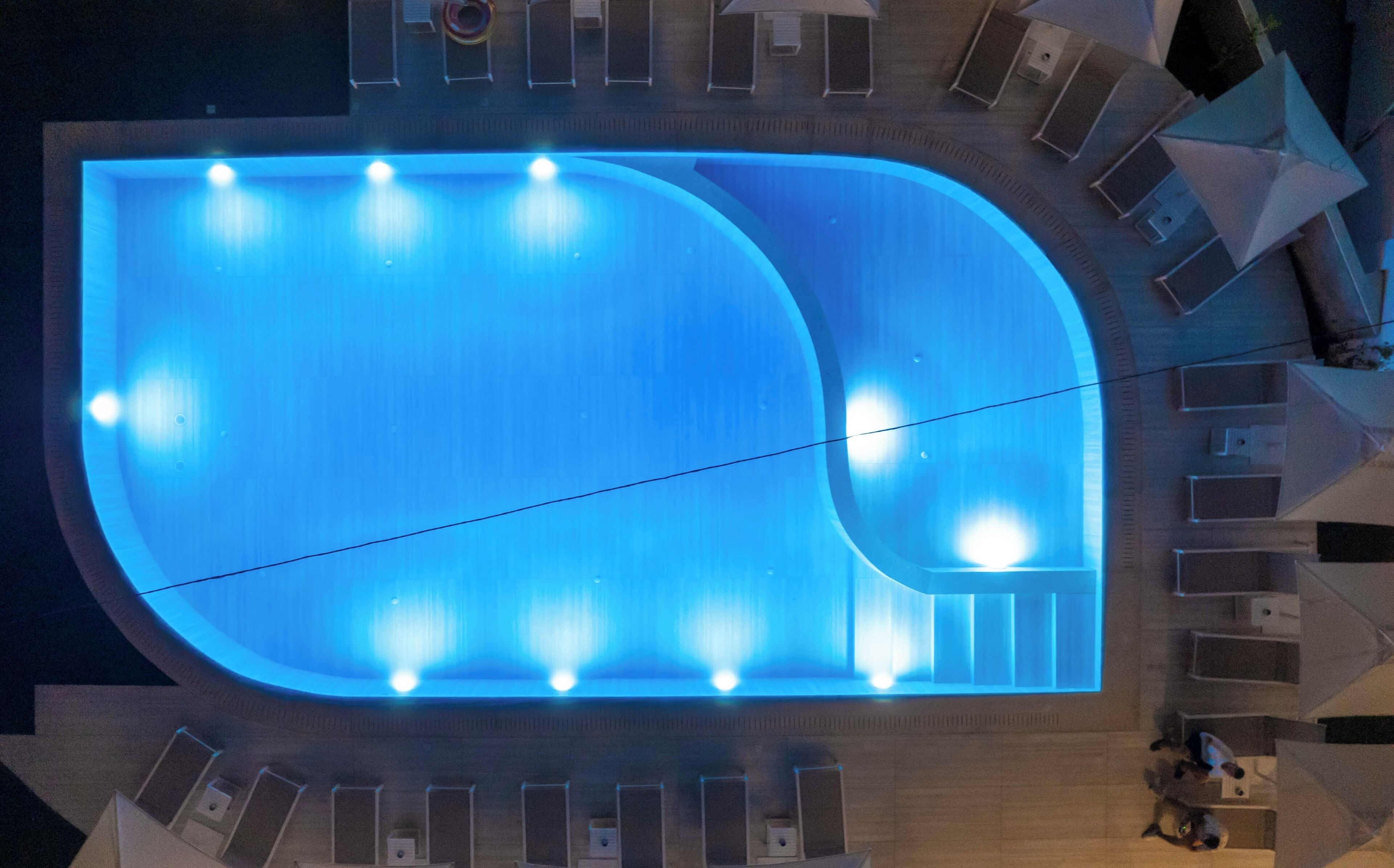 An aerial view of a swimming pool with a curved design, surrounded by lounge chairs and a covered seating area.