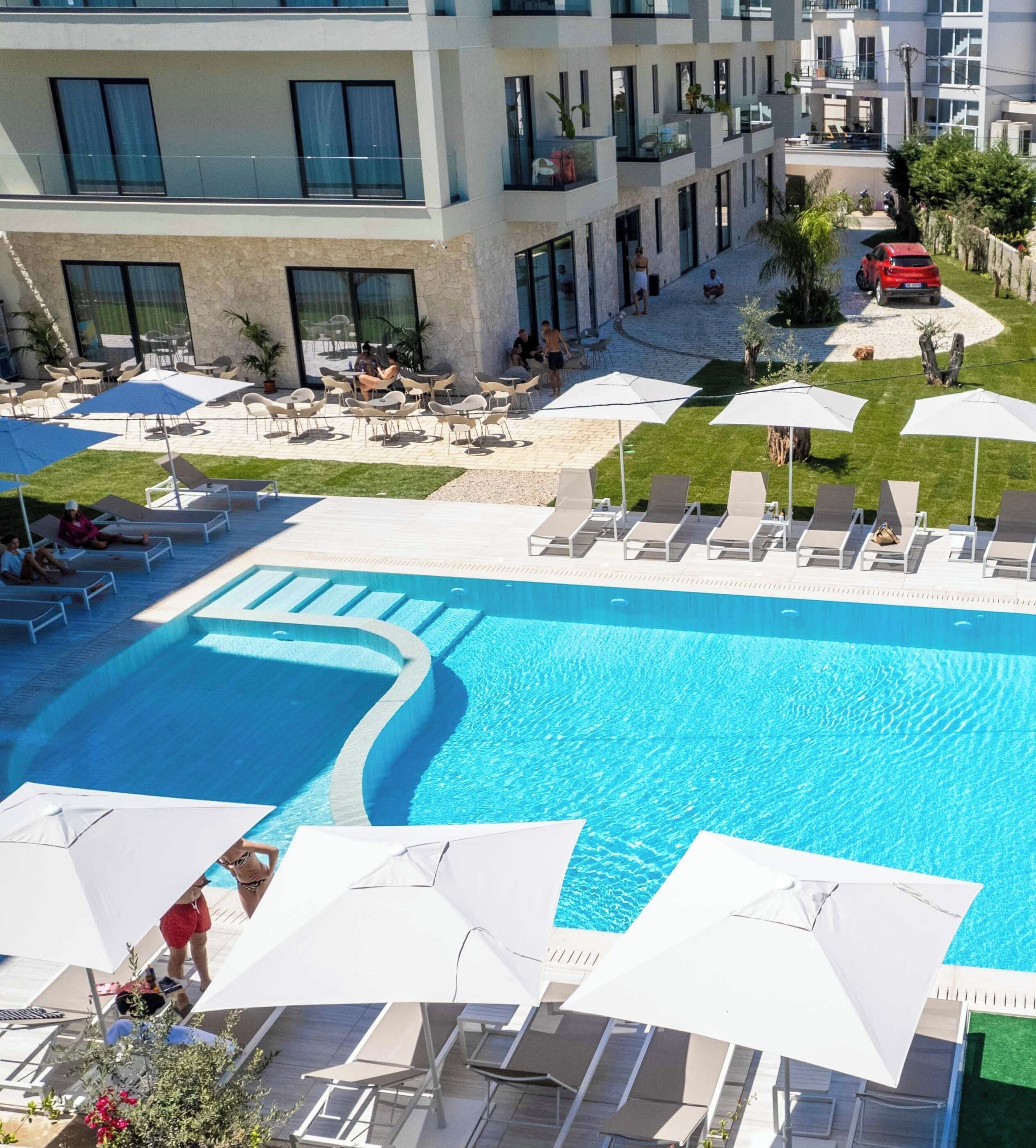 A hotel with a swimming pool, outdoor seating, and a view of the surrounding buildings.
