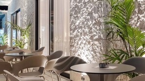 An outdoor seating area with modern chairs and tables, a textured wall, and potted plants. - Sondor Hotel (Ksamil)
