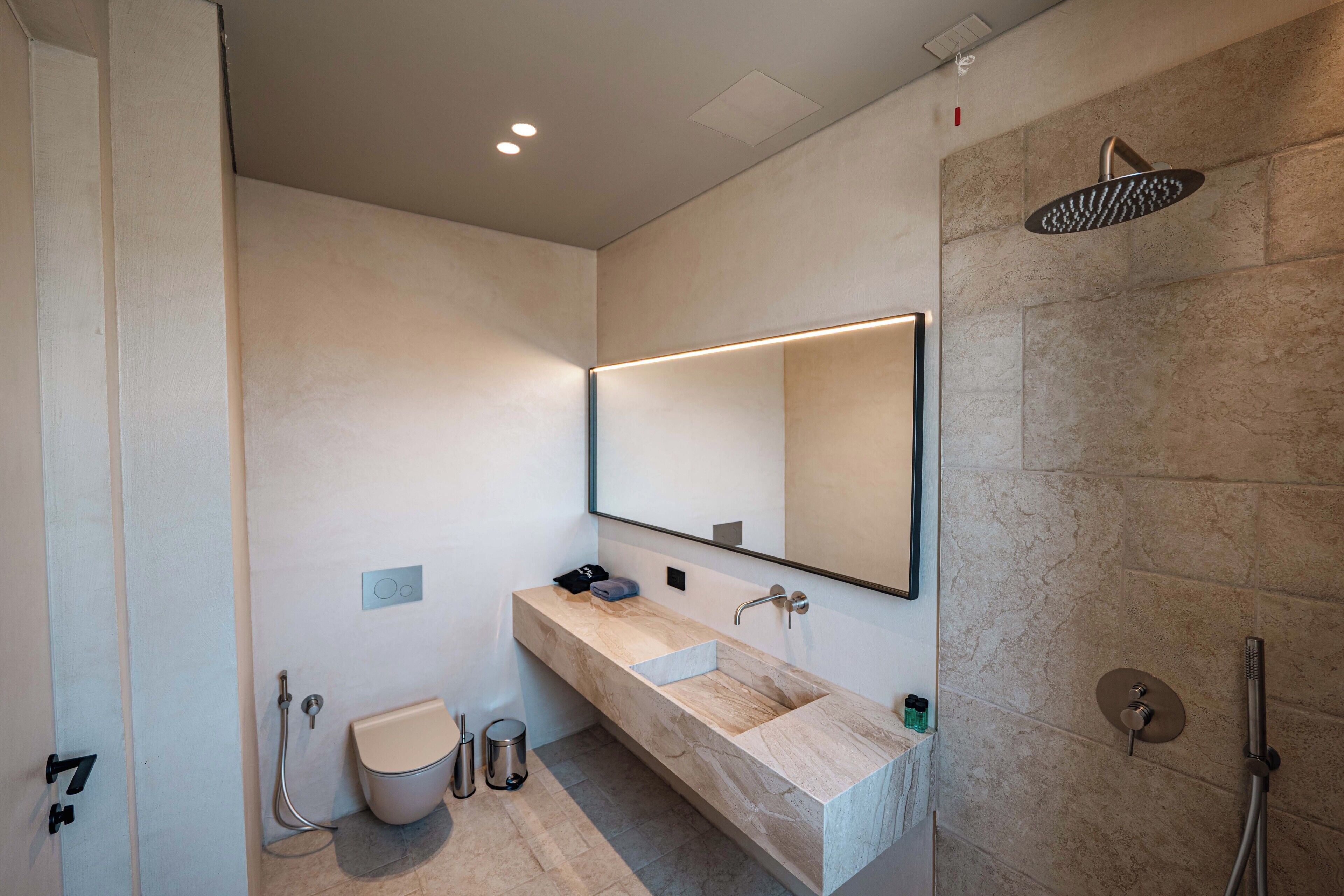 A modern bathroom with a large mirror, a marble sink, a shower, and a toilet.