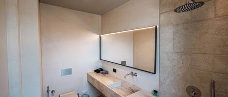 A modern bathroom with a large mirror, a marble sink, a shower, and a toilet.