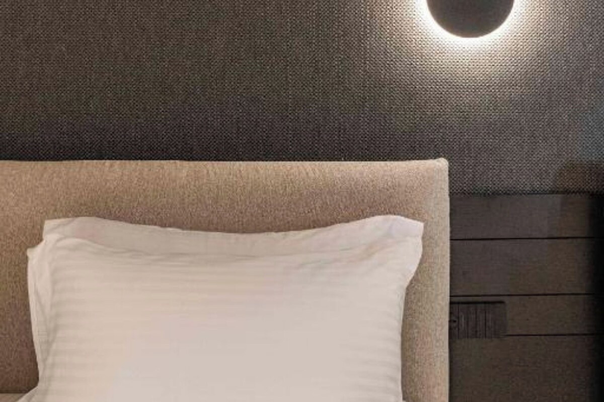 Un lit avec une tête de lit et un luminaire fixé au mur.