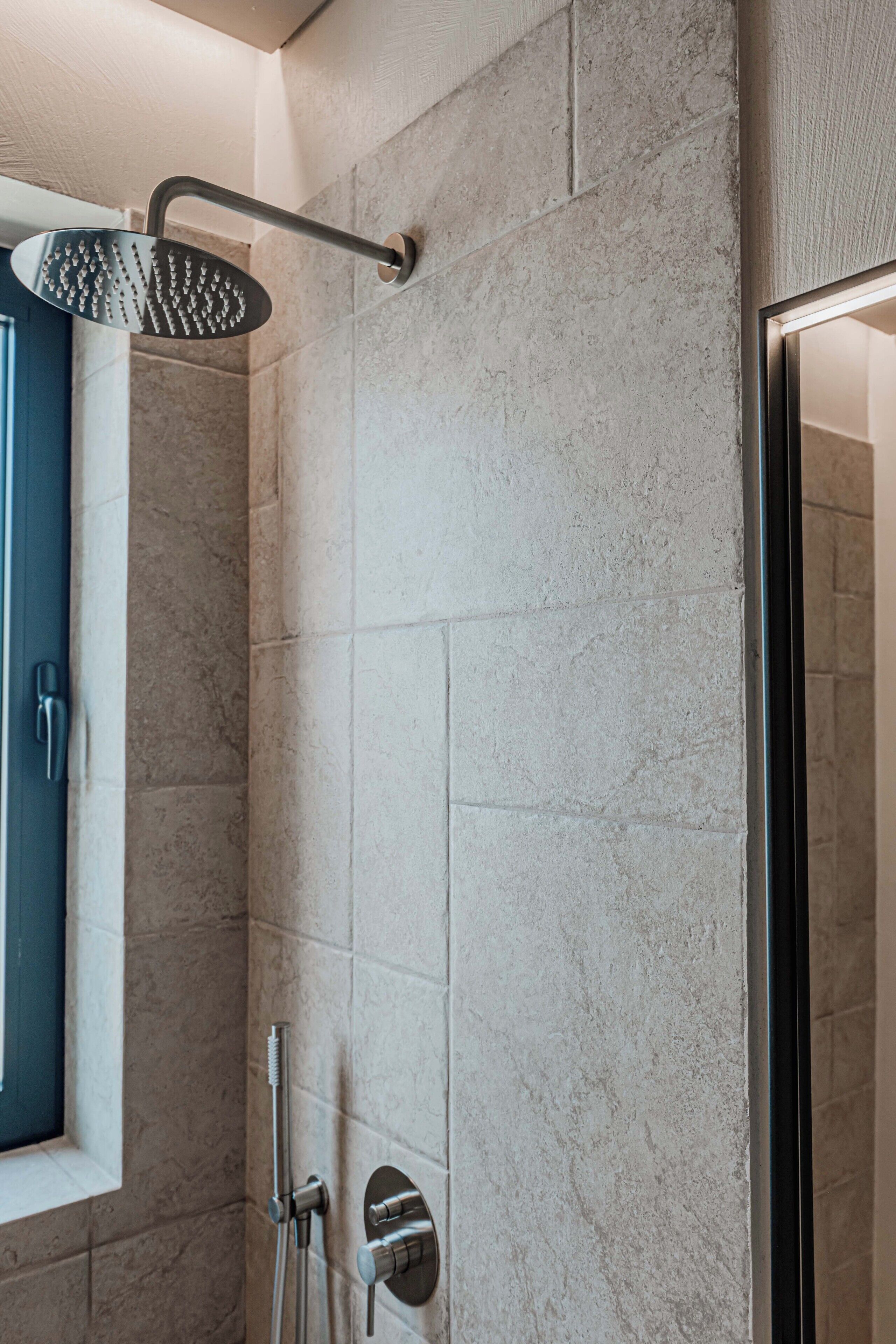 A modern shower with a handheld showerhead and a wall-mounted control.
