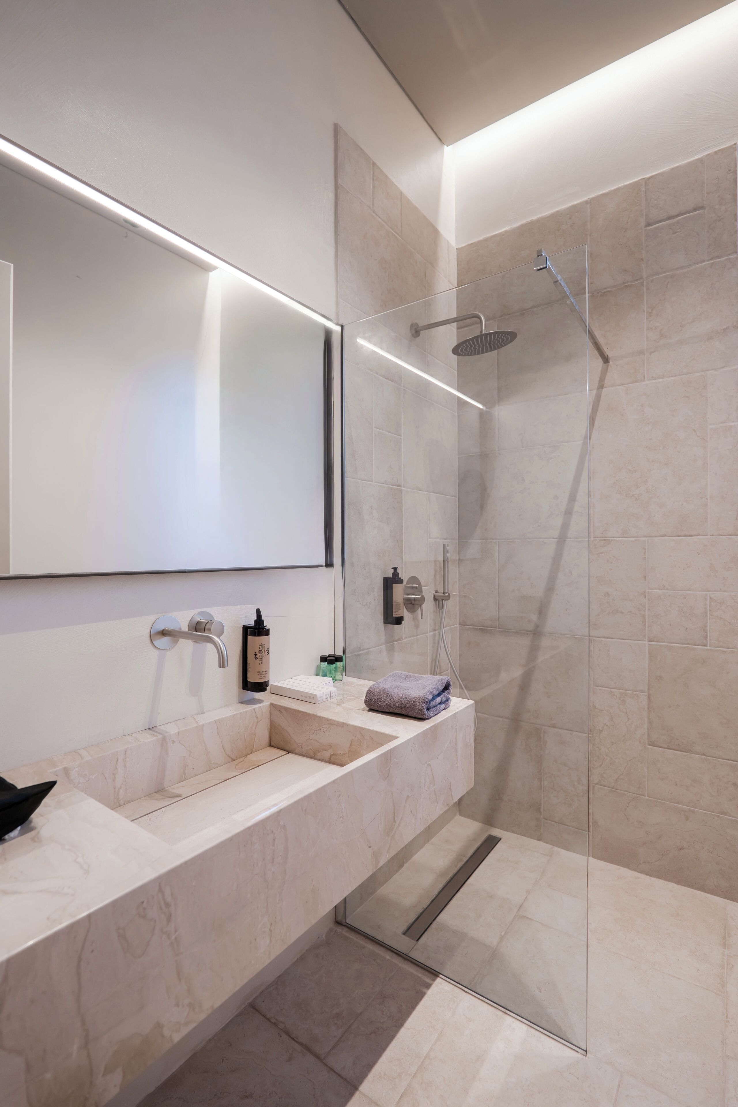 Un baño moderno con un espejo grande, un lavamanos y una ducha con mampara de vidrio.