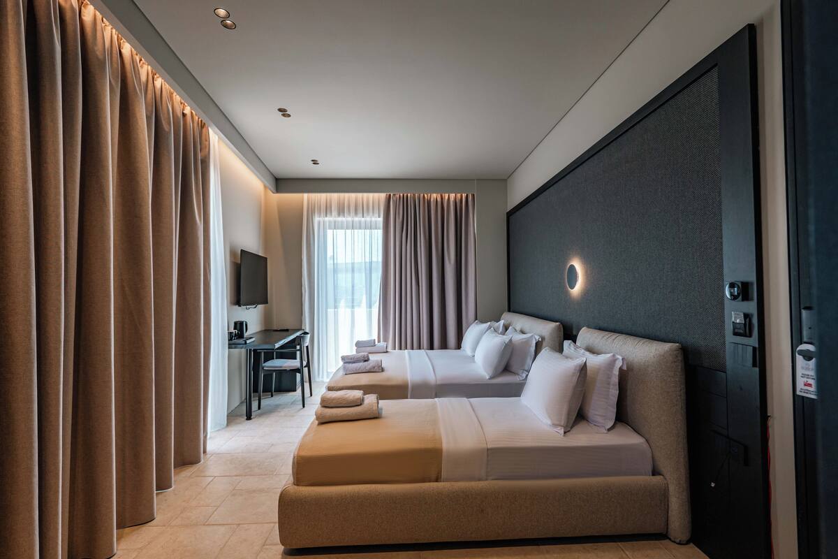 A modern hotel room with two beds, a desk, and a television.