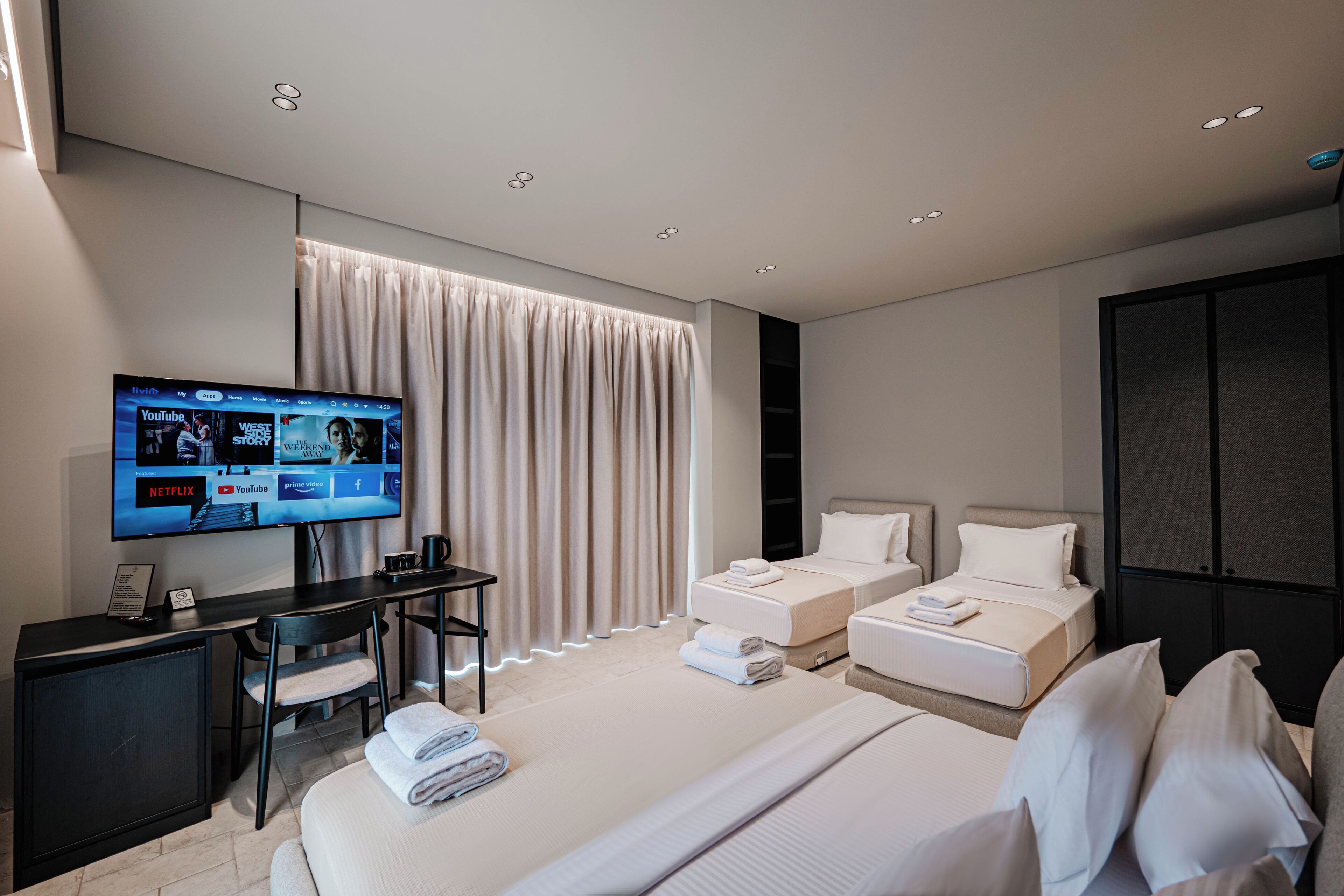 Une chambre d’hôtel moderne équipée d’une télévision affichant l’interface YouTube, d’un bureau avec une chaise, de deux lits et d’une armoire.