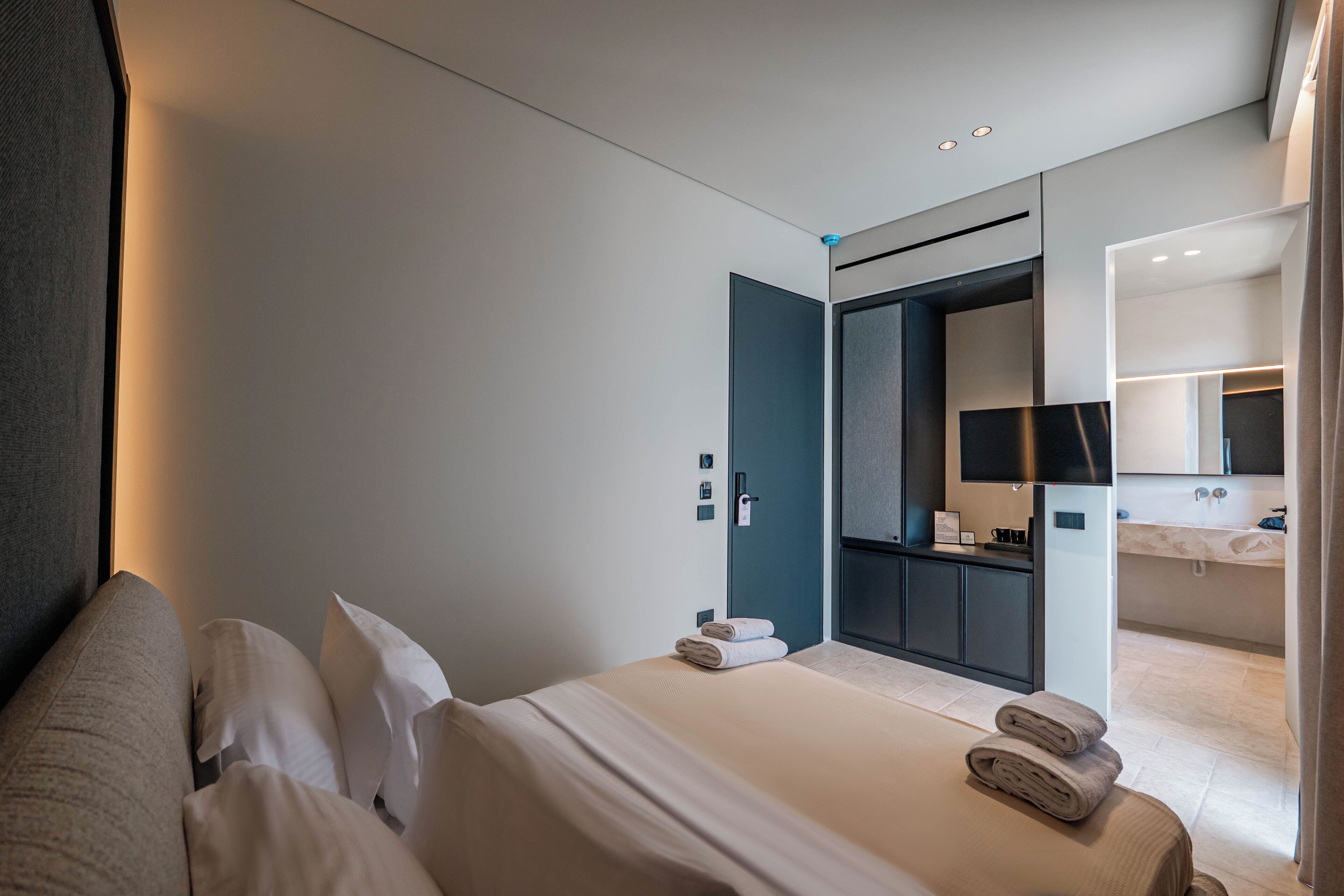 Une chambre d’hôtel moderne dotée d’un grand lit, d’une salle de bain avec un miroir et un lavabo, et d’un dressing.