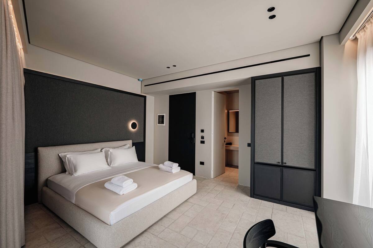 A modern hotel room with a large bed, a desk, and a wardrobe.