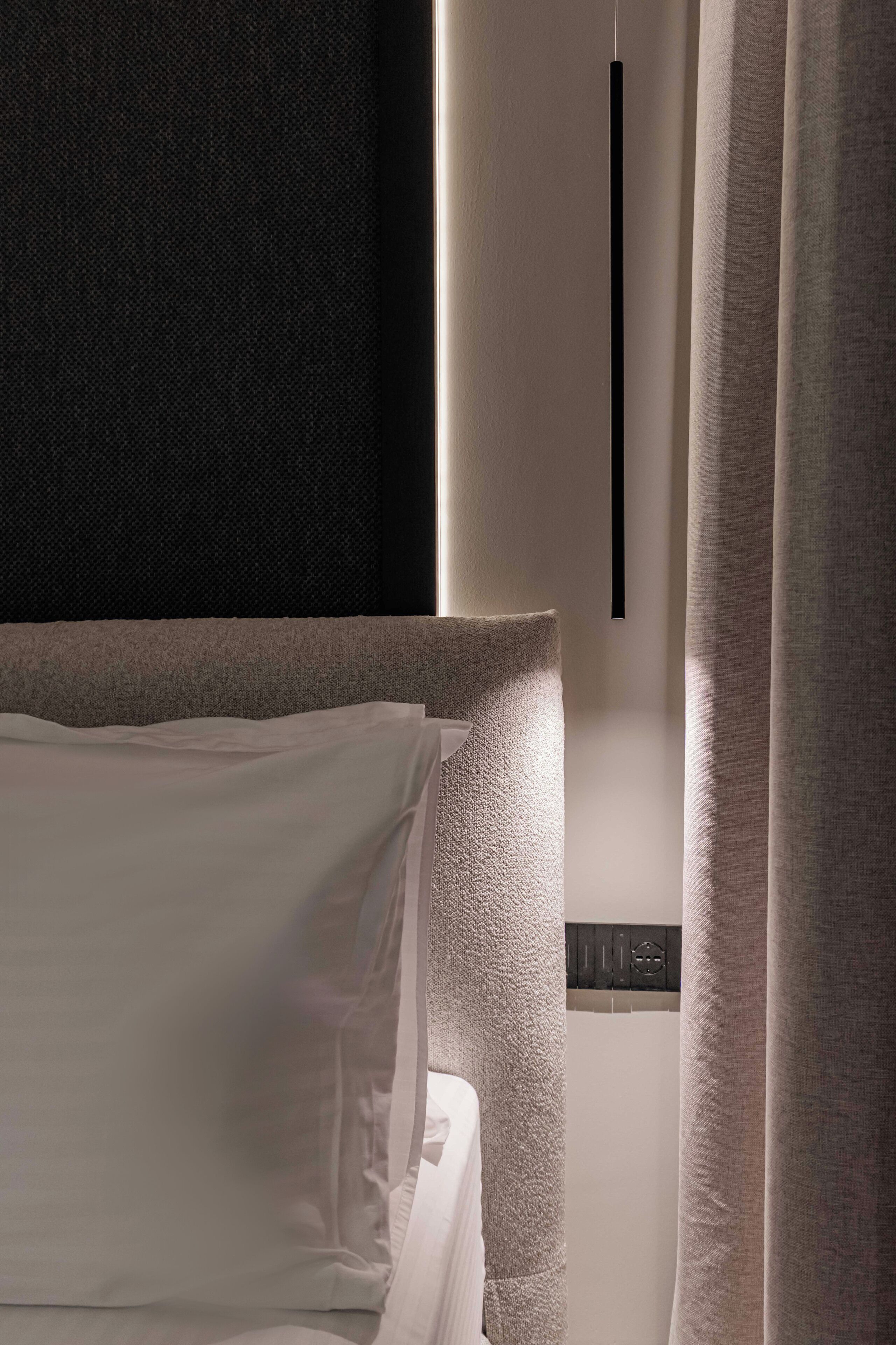 A hotel room with a bed, a headboard, a wall-mounted control panel, and curtains.