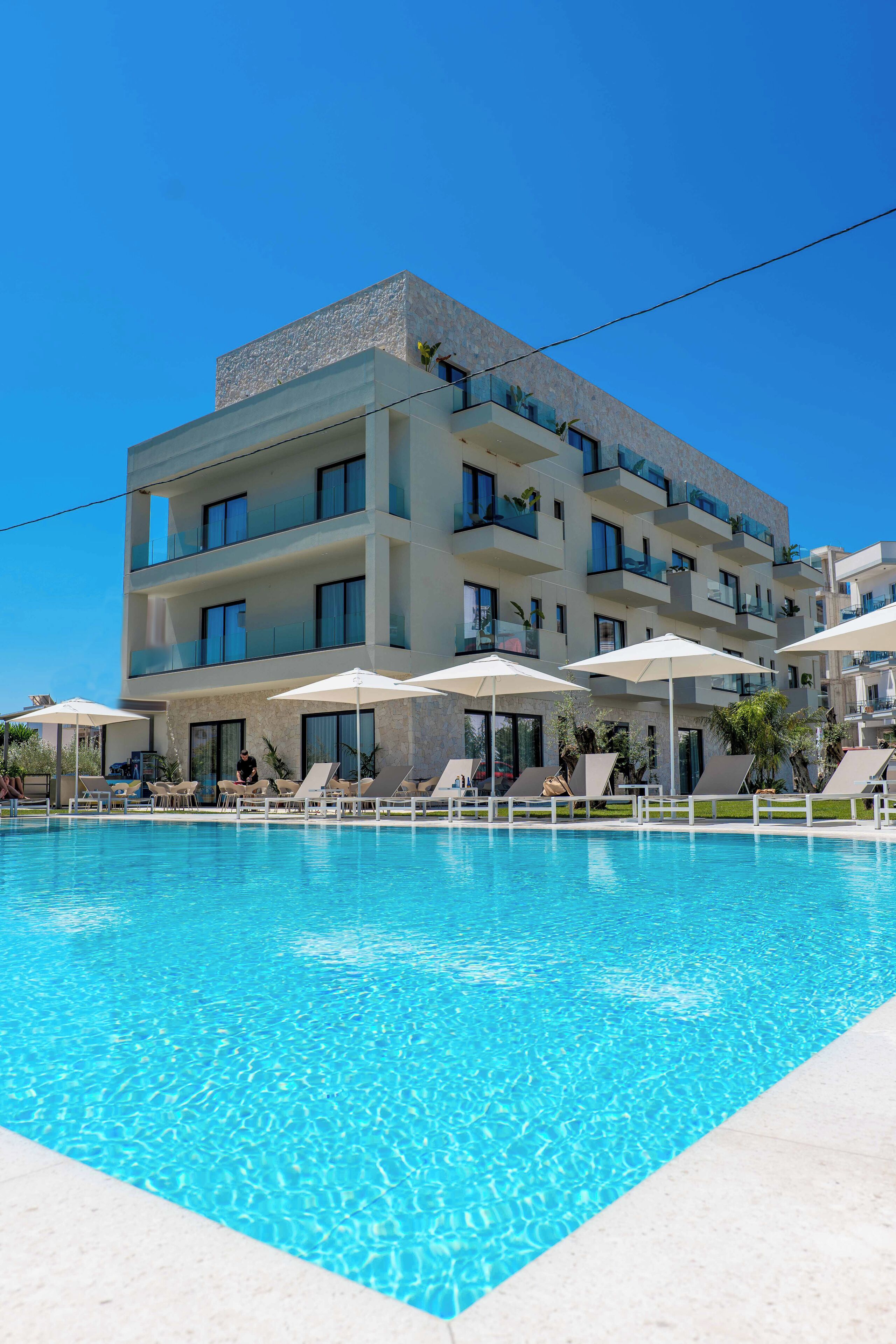 A modern hotel with a swimming pool, multiple balconies, and sun loungers.