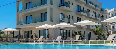 A modern hotel with a swimming pool, multiple balconies, and sun loungers.