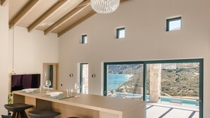 A modern kitchen with a large island, bar stools, and a view of the sea. - Electra Zolla Villa (Zola Village)