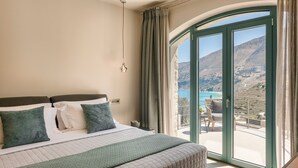 A bedroom with a large bed, a view of a mountainous landscape through a glass door, and a balcony with a chair. - Electra Zolla Villa (Zola Village)