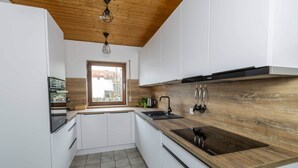 Une cuisine moderne avec des meubles blancs, un plan de travail en bois, une cuisinière encastrée et une fenêtre donnant sur un jardin.