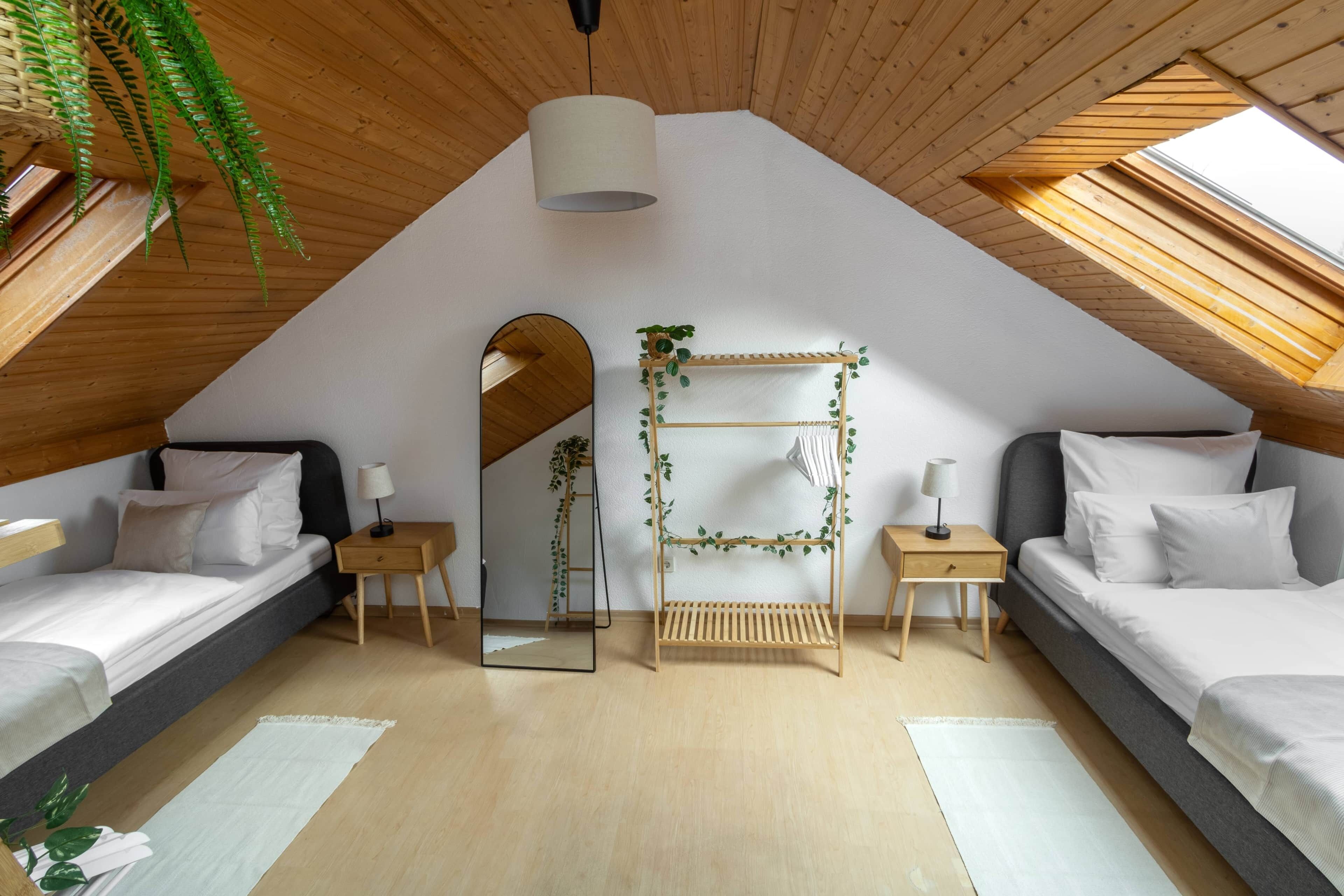 Un dormitorio con dos camas, un tragaluz, un espejo y una estantería de madera con plantas.