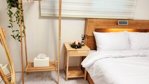 Ein ordentlich eingerichtetes Hotelzimmer mit einem hölzernen Kopfteil, einem Nachttisch mit einer Uhr, einer Zimmerpflanze und einem Bett mit weißen Leinen.