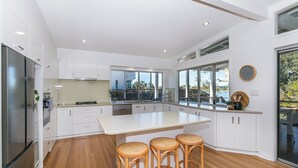 Una cocina moderna con armarios blancos, una isla grande y tres taburetes de mimbre.