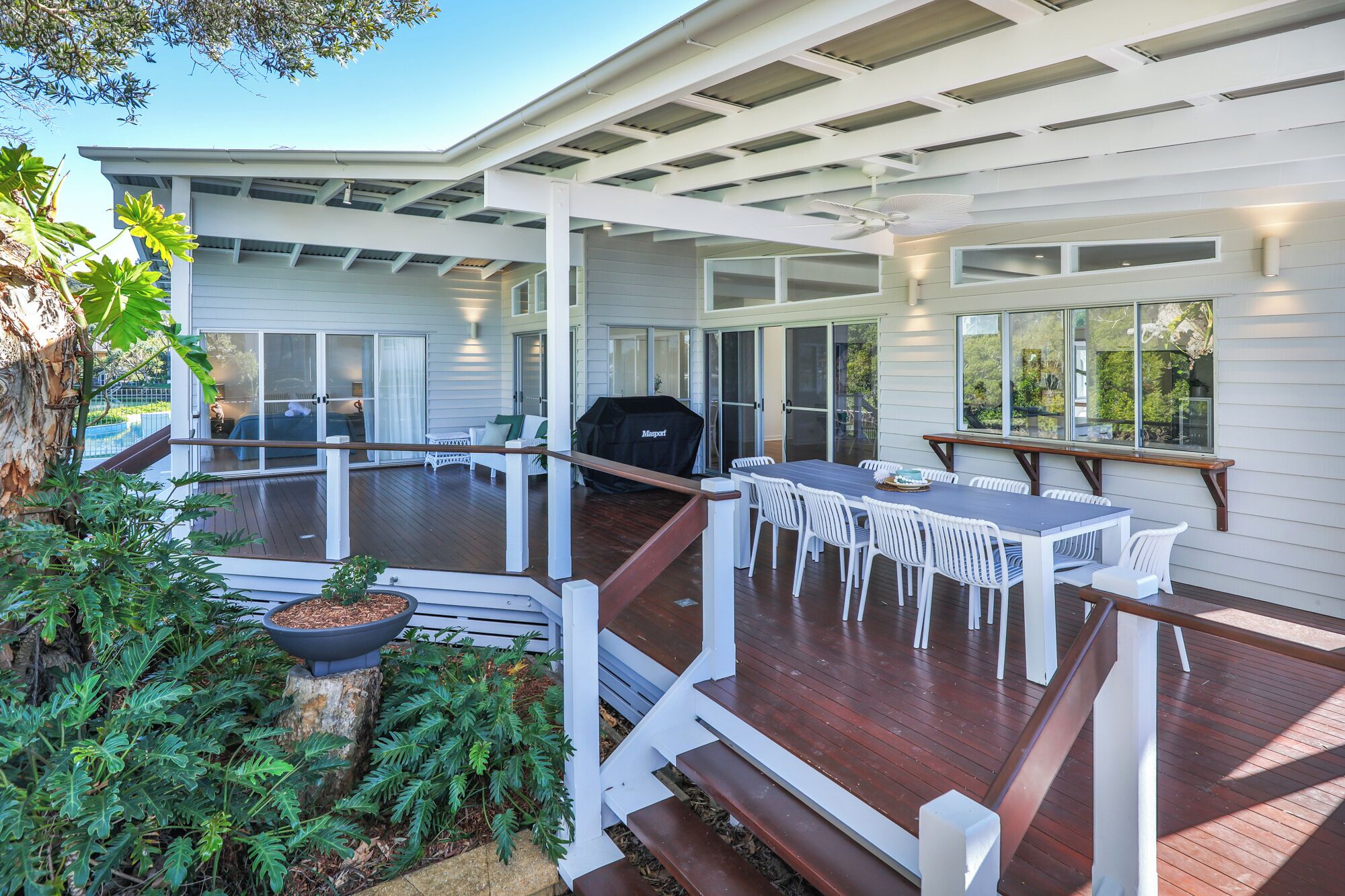 Una terraza techada al aire libre con una parrilla, una mesa de comedor con sillas y una escalera que lleva a un segundo nivel.