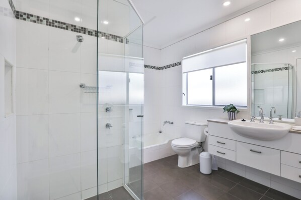 Un baño moderno con cabina de ducha de vidrio, inodoro blanco, bañera y tocador con lavamanos y espejo.