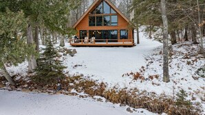 Una cabaña con un amplio ventanal, rodeada de árboles y nieve.
