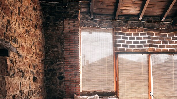 A bedroom with a large bed, a bench, a stone wall, and a wooden ceiling.