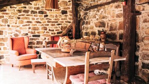 A rustic dining area with a wooden table and chairs, a stone wall, and hanging wooden lamps.