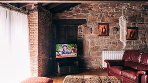 A rustic living room with exposed wooden beams, a stone wall, a television, a leather sofa, and a wooden coffee table.