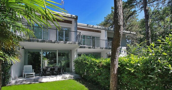 A modern two-story house with a balcony, large windows, and a well-maintained garden.