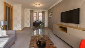 A modern living room with a sofa, a glass coffee table, a TV, and a dining area with a table and chairs. - Coastal Aprt in Anstruther -sleeps4 -Tv - Wifi (Anstruther)