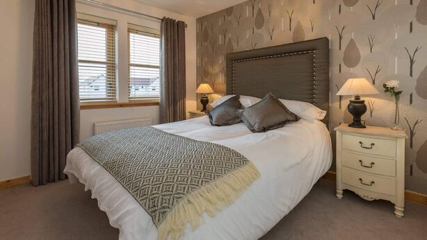 A bedroom with a large bed, a nightstand with a lamp, and a window with curtains. - Coastal Aprt in Anstruther -sleeps4 -Tv - Wifi (Anstruther)