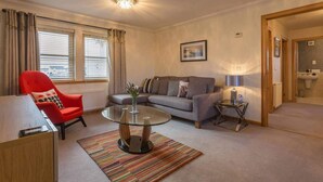 A living room with a sofa, a red chair, a glass coffee table, a striped rug, and a lamp. - Coastal Aprt in Anstruther -sleeps4 -Tv - Wifi (Anstruther)