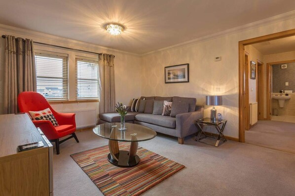 A living room with a sofa, a red chair, a glass coffee table, a striped rug, and a lamp. - Coastal Aprt in Anstruther -sleeps4 -Tv - Wifi (Anstruther)