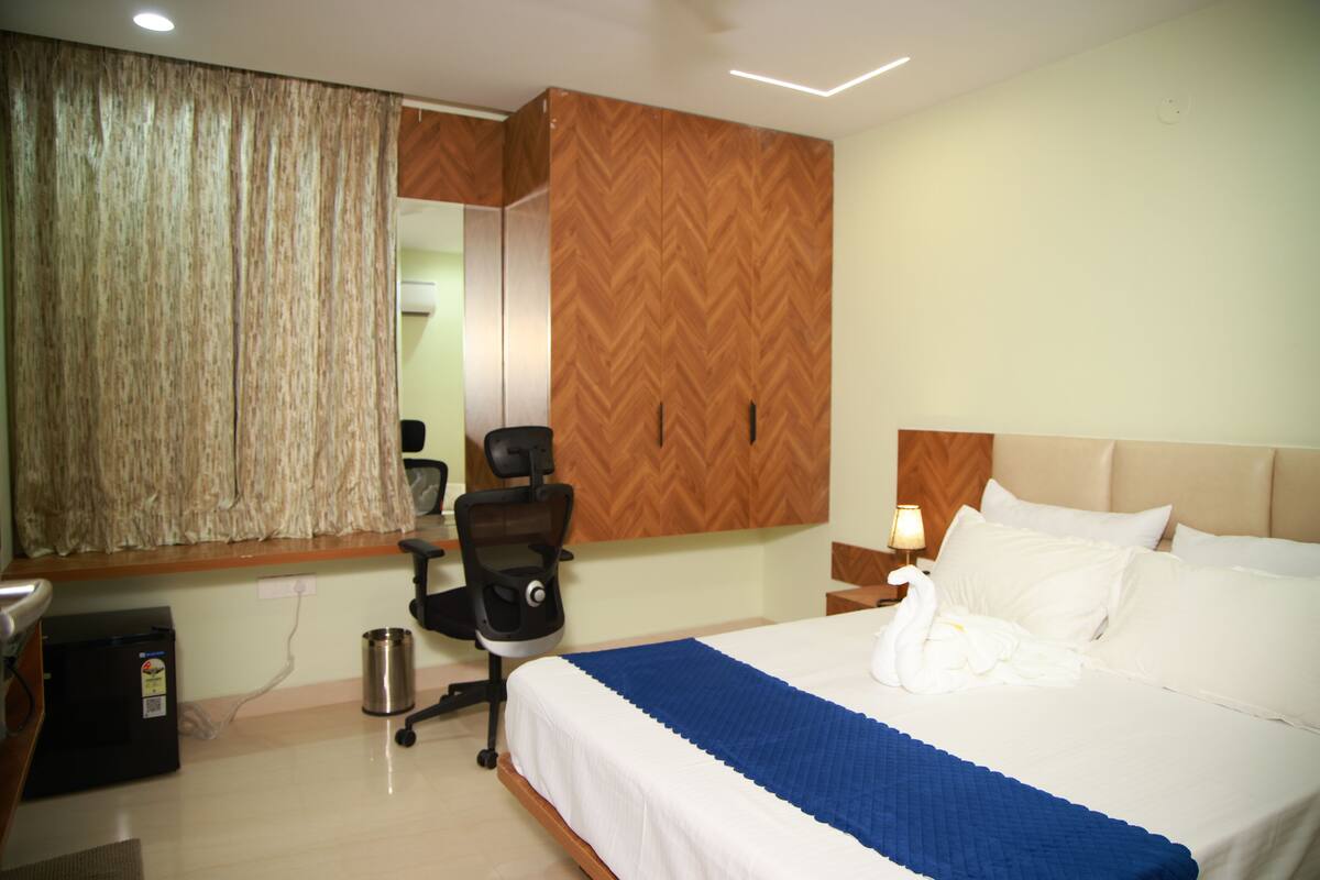 A hotel room with a bed, a desk, a chair, a mirror, and a wall-mounted heater.