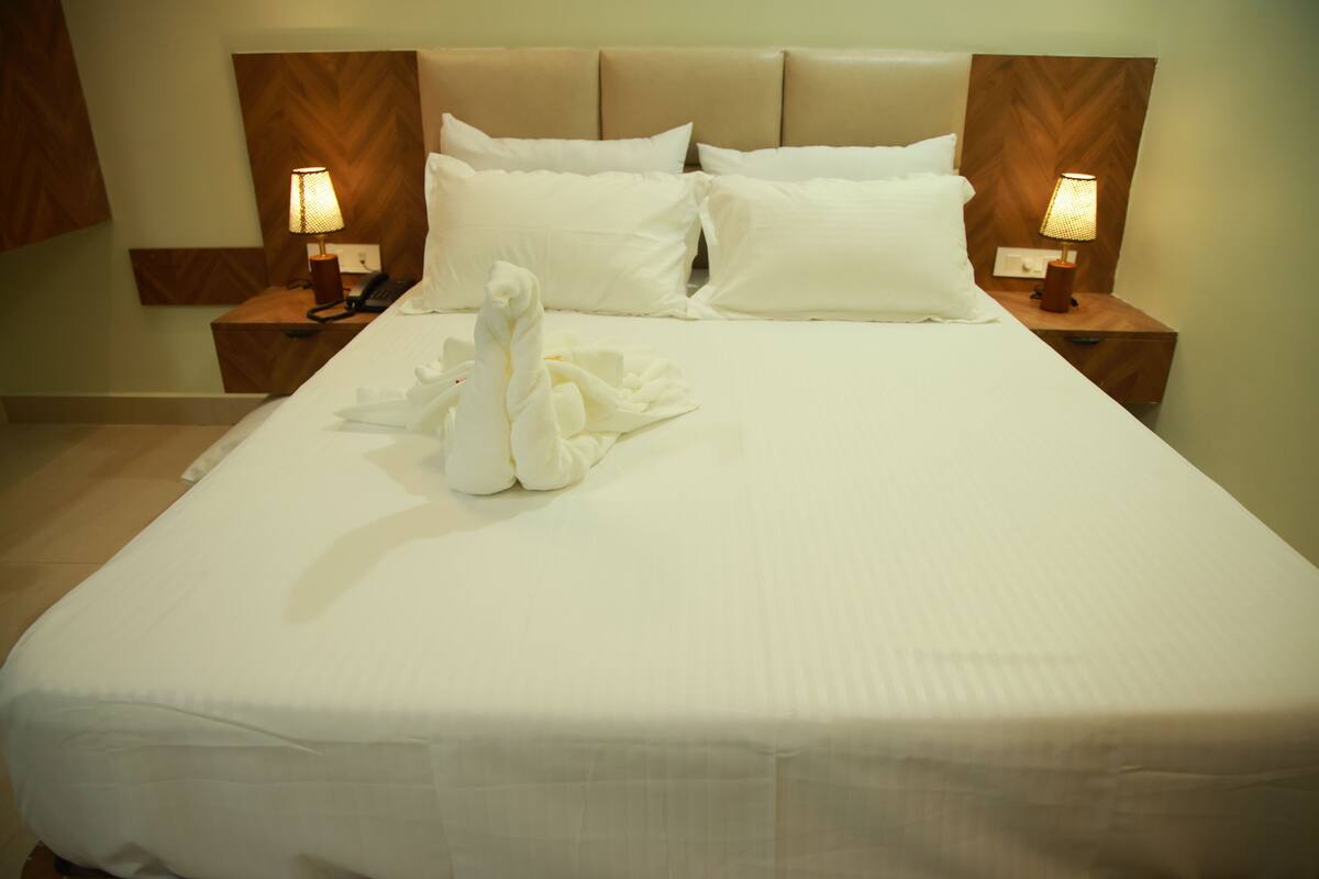 A neatly made bed with white linens, two bedside lamps, and a decorative swan towel arrangement.