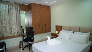 A hotel room with a bed, a desk, a chair, a lamp, a trash bin, and a mirror.