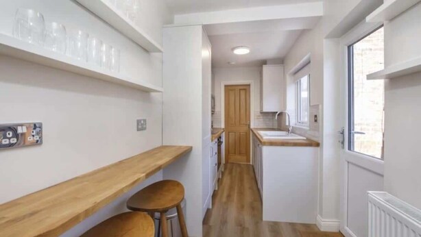 Una cucina angusta con mobili bianchi, un piano di lavoro in legno e una finestra.