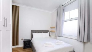 Un letto ben rifatto con lenzuola bianche, una testata grigia e un comodino con una lampada.