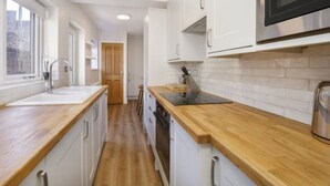 Cucina con mobili bianchi, piani di lavoro in legno, microonde in acciaio inox e una finestra che offre luce naturale.