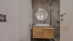 Un baño moderno con lavamanos blanco, tocador de madera, espejo redondo y cabina de ducha de vidrio.