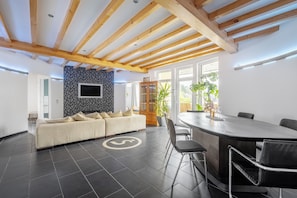 A modern interior with a sofa, dining table, chairs, a TV, and a large window.