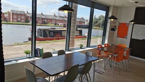 A dining area with a view of a river and boats, featuring a wooden table and modern chairs. - Student Only The Towpath (Chester)