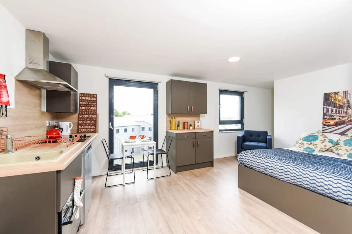 Una habitación de hotel compacta con kitchenette, comedor y cama.
