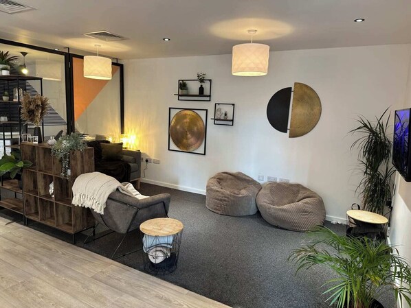 A modern living room with a sofa, two bean bags, a coffee table, and a TV mounted on the wall.