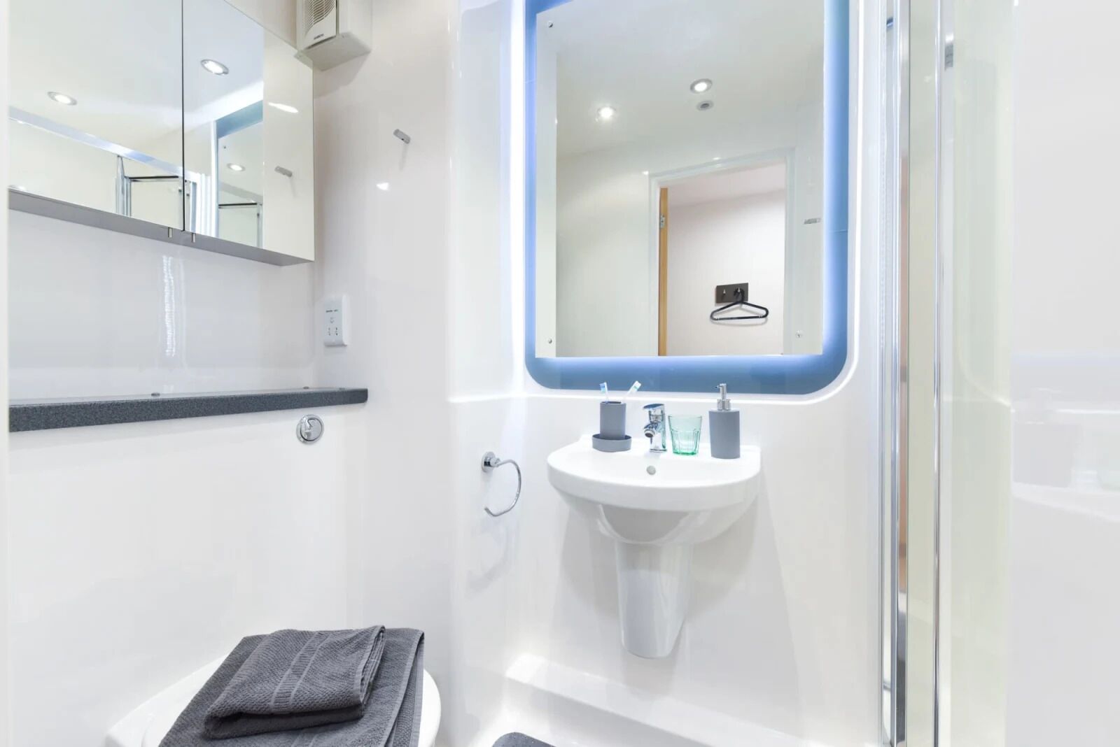 A modern bathroom with a white sink, a mirror, and a towel on a stool.